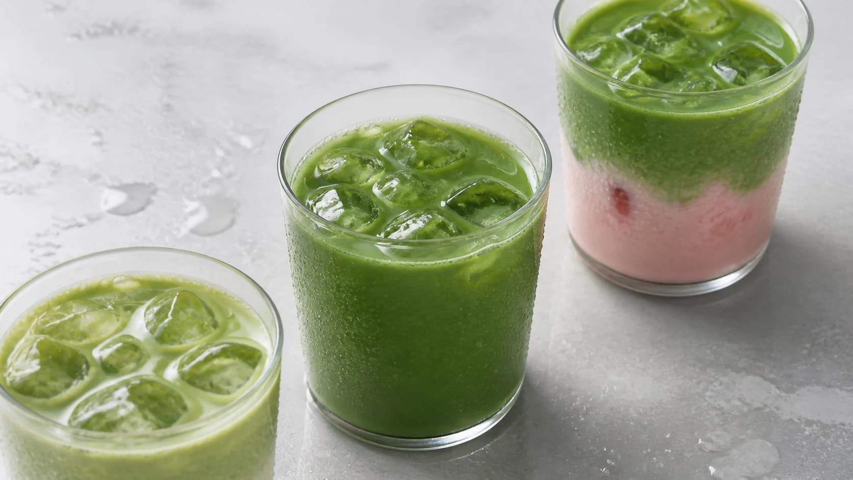 Three iced matcha drinks arranged on a pale stone surface